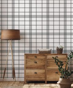 a wooden dresser sitting next to a lamp on top of a hard wood floor in front of a plaid wallpaper