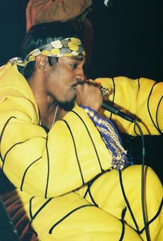 a man sitting on top of a chair while holding a microphone in his hand and wearing a yellow outfit