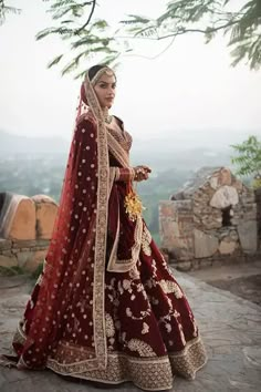 a woman in a red and gold bridal gown is standing on a stone walkway