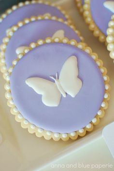 purple and white cupcakes with butterfly decorations on them are sitting on a table