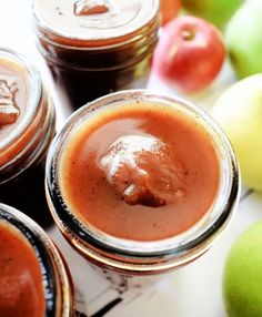 three jars filled with brown liquid next to apples