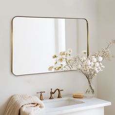 a bathroom sink with a mirror above it and flowers in the vase on the counter