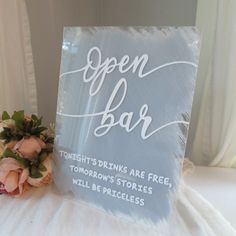 an open bar sign sitting on top of a bed next to a bouquet of flowers