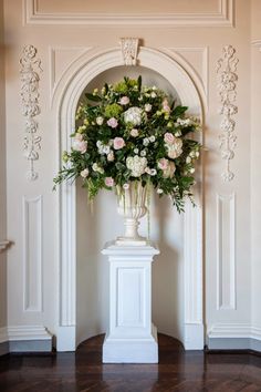 a vase filled with lots of flowers on top of a white pedestal next to a wall