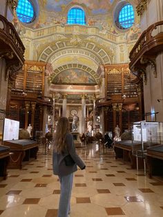 a woman standing in the middle of a room with many bookshelves and windows