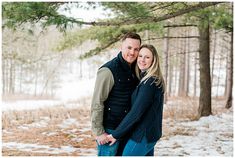 a man and woman standing next to each other in front of snow covered ground with trees