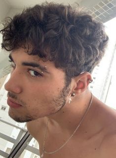 a young man with curly hair and no shirt looking at something in the distance while standing next to a window