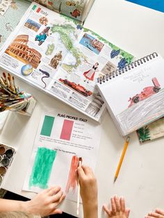 two children are doing crafts on a table with books and watercolor pencils in front of them