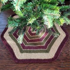 a crocheted pot holder is sitting on a wooden table next to a pine tree