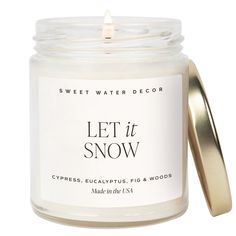 a white candle with the words let it snow written in black on it and a gold lid