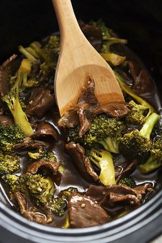 broccoli and mushrooms are being cooked in the crock pot with a wooden spoon