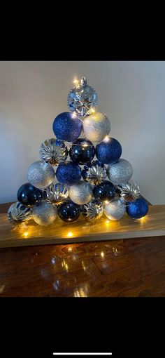 a blue and silver christmas tree with lights on it's top is sitting on a wooden table