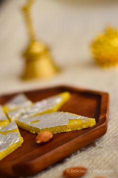 two pieces of yellow and white cake on a wooden plate with gold decorations in the background