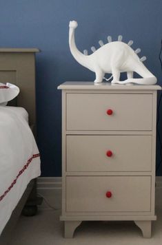 a white toy dinosaur sitting on top of a dresser next to a bed with blue walls