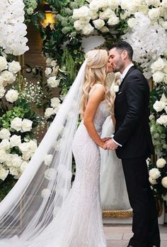 a bride and groom kissing in front of a floral arch at their wedding ceremony with white flowers