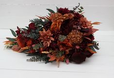 the bridal bouquet is made up of red and orange flowers, greenery, and leaves