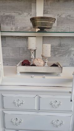 a white dresser with two candles on top and some other items in the bottom drawer