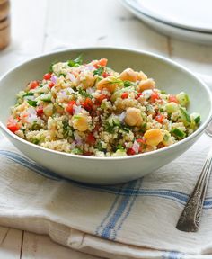 a white bowl filled with rice and vegetables on top of a blue towel next to a fork