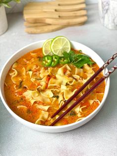 a white bowl filled with soup and chopsticks on top of a table next to some lemon wedges