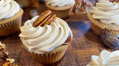 cupcakes with white frosting and pecans on the side sitting on a wooden table