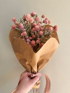 a person holding a bunch of flowers in their hand and tied with a pink ribbon