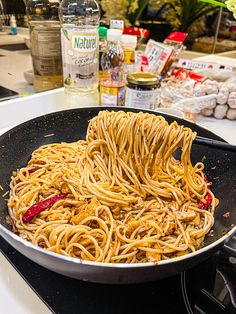 noodles being cooked in a wok on the stove top with spices and condiments