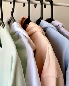 several folded shirts hanging on a rack in front of a white wall with black hooks