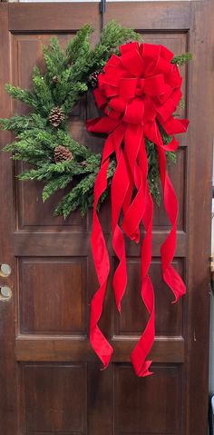 a christmas wreath on the front door of a house with red ribbon and pine cones