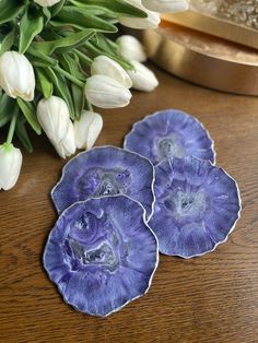 three purple flowers sitting on top of a wooden table next to white tulips