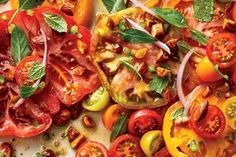 sliced tomatoes and other vegetables on a cutting board with basil leaves, olives, and seasonings