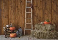 hay bales and pumpkins are arranged in front of a wooden wall with a ladder