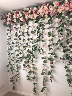 the wall is covered with pink flowers and greenery hanging from it's sides