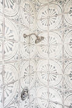 the shower head is attached to the wall with an intricate pattern on it's tile