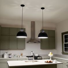 two lights hanging over a kitchen island in a room with green cabinets and white counter tops