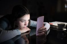 a woman looking at her phone while sitting in front of a cup