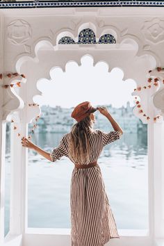 a woman in a striped dress and hat looking out at the water from an archway