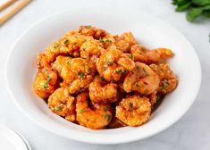 a white bowl filled with shrimp and garnished with parsley next to chopsticks