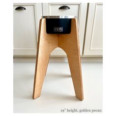 a wooden stool with a black electronic device on it's legs in front of white cabinets