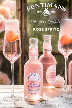 three bottles and two wine glasses sitting on a table with pink flowers in the background