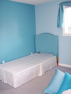 a bed sitting in the middle of a bedroom next to a window with blue walls