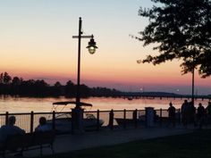 people sitting on benches near the water at sunset