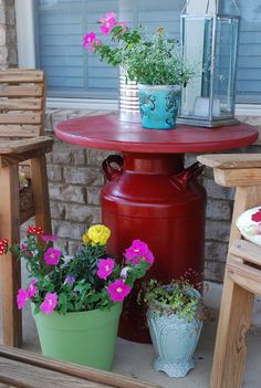 a red table and chairs with potted flowers on it next to a brick wall