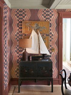 a sailboat is sitting on top of a dresser in a room with red and blue wallpaper