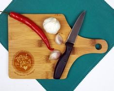 a cutting board with a knife and some garlic on it next to a red pepper