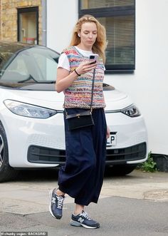 a woman is looking at her phone while walking down the street in front of a car