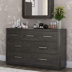 a dresser with a large mirror above it and some items on top of it in front of a floral wallpapered wall