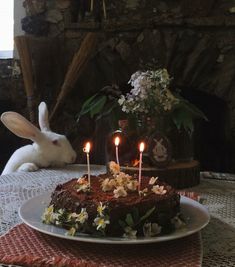 a rabbit is sitting in front of a cake with lit candles on it and flowers