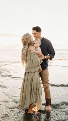 a man and woman standing on the beach with their baby girl in her arms, holding him