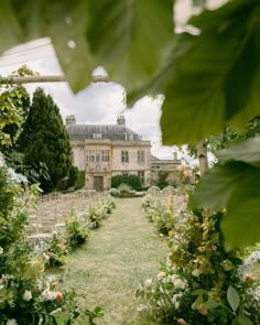 a large house surrounded by lush green trees and flowers in the foreground is a garden with lots of greenery