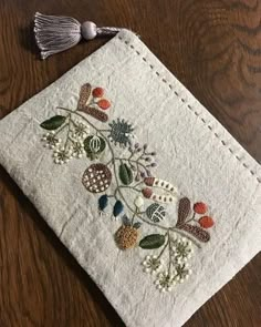 an embroidered piece of cloth sitting on top of a wooden table next to a tassel